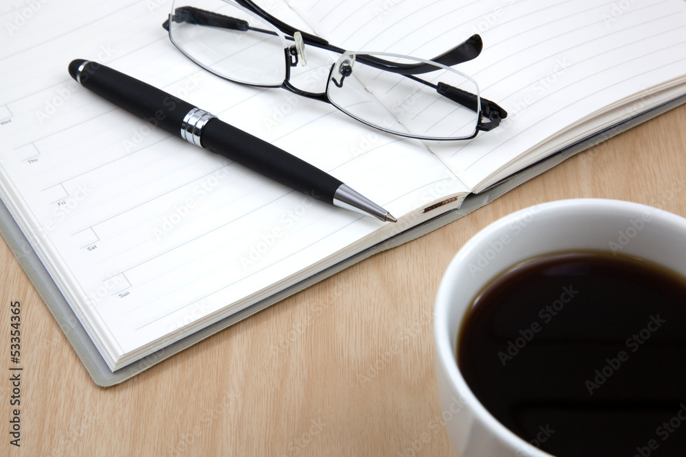 Cup of coffee on a wooden table with book and pen Cup of coffee on a wooden table with book and pen