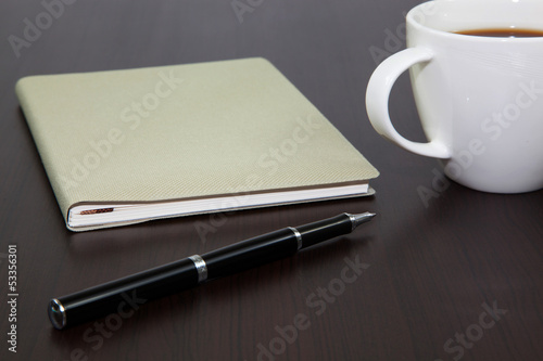 Cup of coffee on a wooden table with book and pen