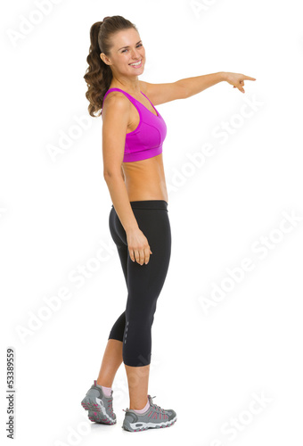 Full length portrait of fitness woman pointing on copy space