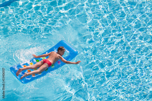 A boy floats on an inflatable mattress in pool face down
