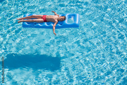 boy floats on an inflatable mattress in pool face up