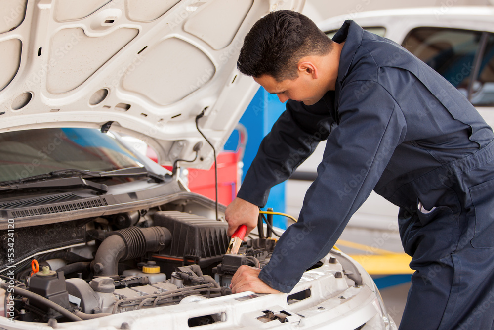 Mechanic using jumper cables to start a car in an auto shop