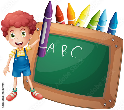 A little boy holding a big violet crayon near the blackboard