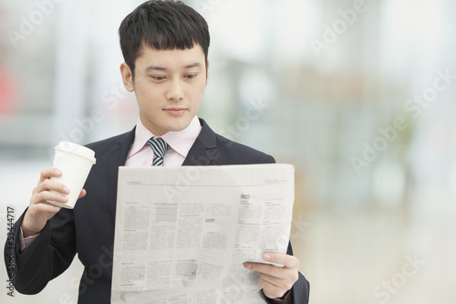 Photography Young business man holding coffee cup and reading newspaper
