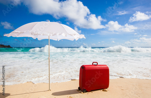 white sunshade and red suitcase at the beach