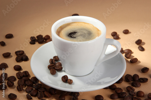 Cup of coffee with coffee beans on beige background