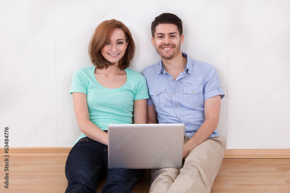 Portrait of young happy couple sitting on floor using laptop