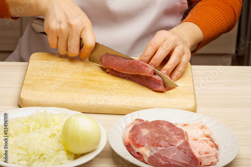 Closeup of woman hands cutting beef on cutting board.