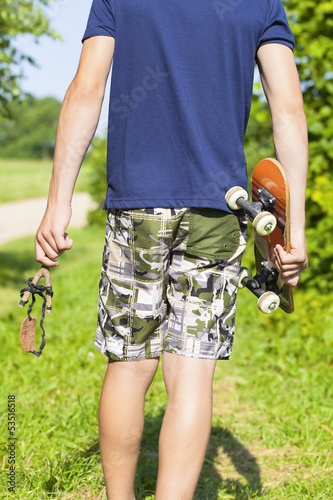 Boy with a slingshot and skateboard on rural road