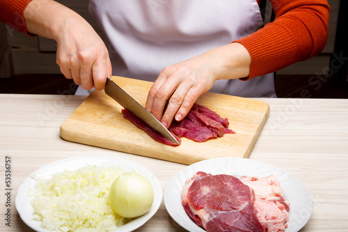 Closeup of woman hands cutting beef on cutting board.