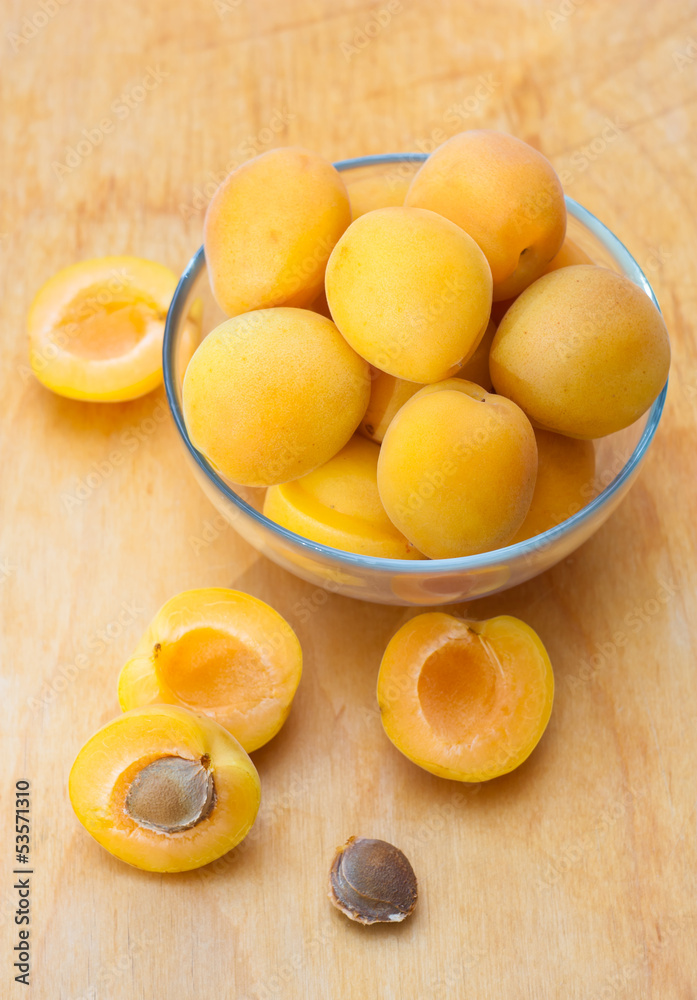 Ripe apricots in glass bowl on wooden board