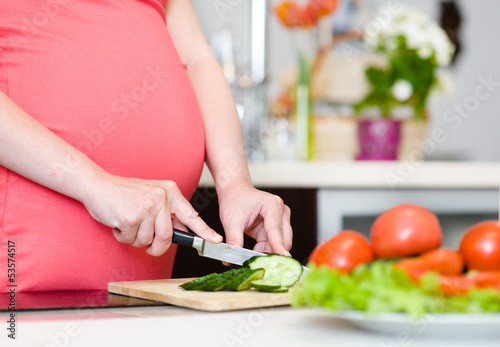 Close up pregnant woman with knife on kitchen cuts cucumber