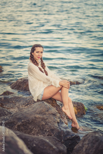 Beautiful young woman sitting on the stone on the seashore