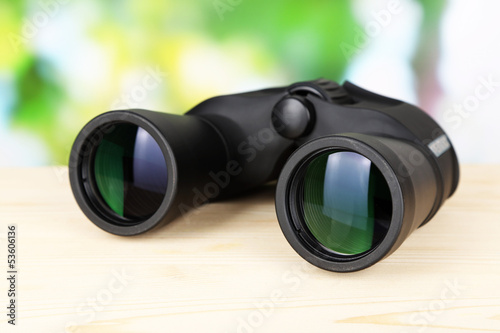 Black modern binoculars on wooden table on green background