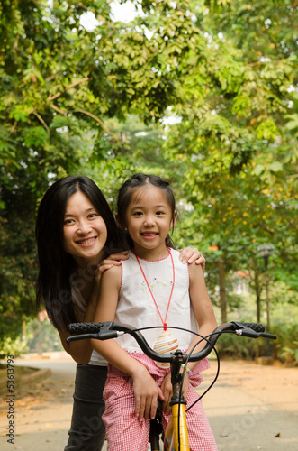 asian chinese mother teaching her daughter riding bicycle outdoo