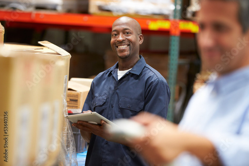 Manager In Warehouse With Worker Scanning Box In Foreground