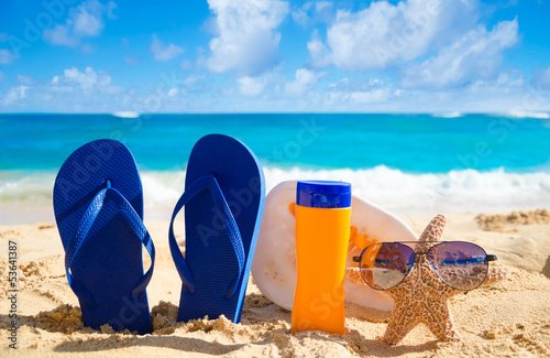 Flip flops, seashell, sunscreen and starfish with sunglasses on