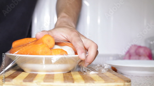 Closeup of wrapping plate of root vegetable with plastic foil