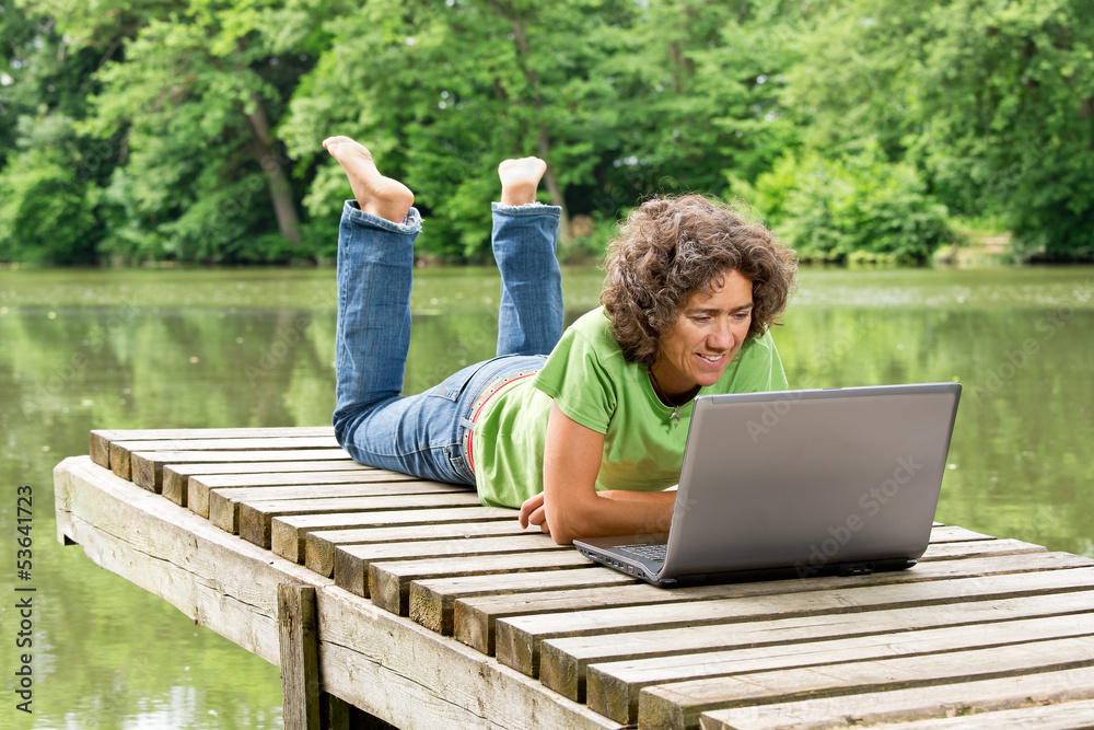 Fototapeta premium Frau mit Notebook am idyllischen Teich - Home Office