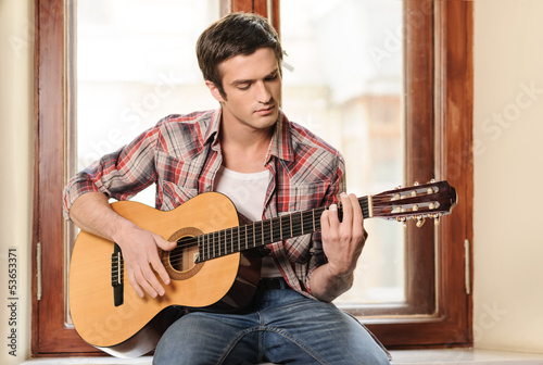 Men playing guitar. Handsome young men sitting on the windowsill