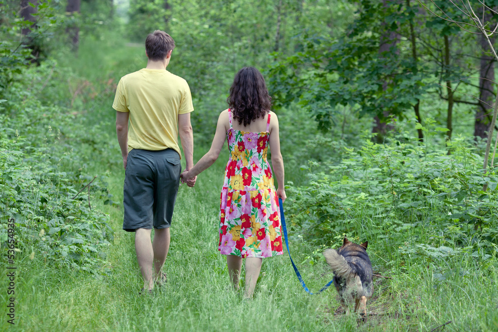 Obraz premium Young couple holding hands and walking with dog in the forest