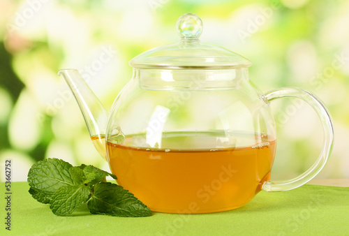 Teapot with mint on table on bright background