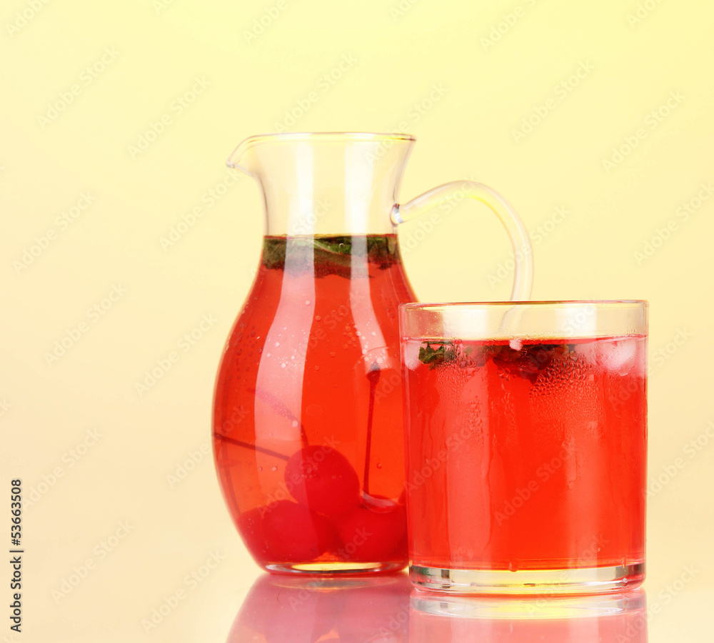 Cherry drink in pitcher and glass on yellow background.