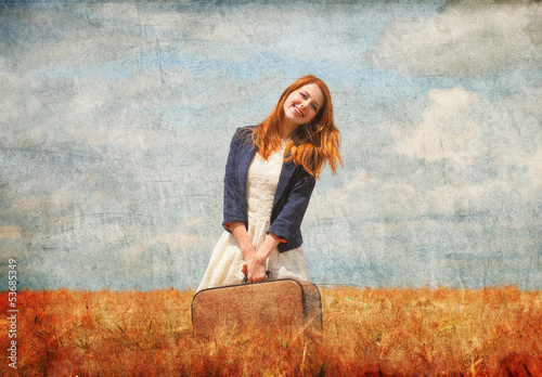 Redhead girl with suitcase at spring wheat field.