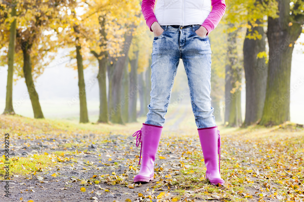 detail of woman wearing rubber boots in autumnal alley detail of woman wearing rubber boots in autumnal alley