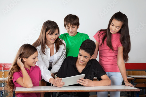 Teenage Schoolboy Showing Tablet To Classmates At Desk