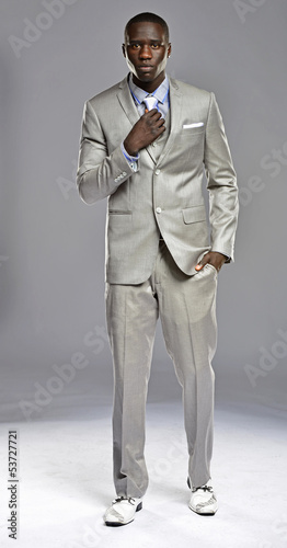 Black man in suit adjusting his tie as he walks