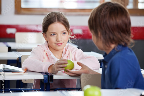 Little Girl Giving Apple To Boy In Classroom