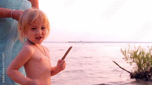 мама заплетает, причёсывает маленькую девочку на пляже