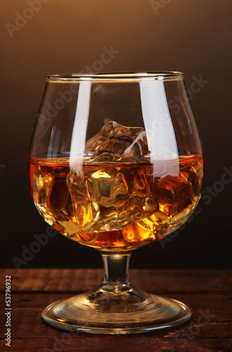 Obraz na plátne Brandy glass with ice on wooden table on brown background