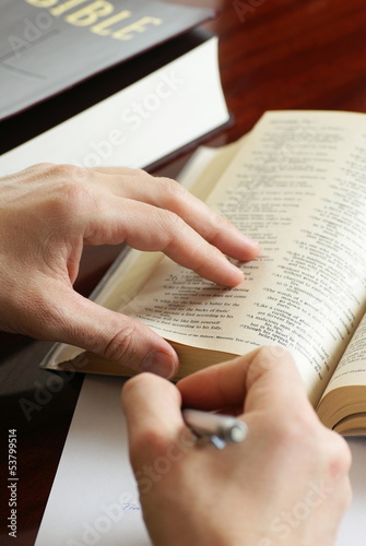 Detail of hands with pen and open Bible