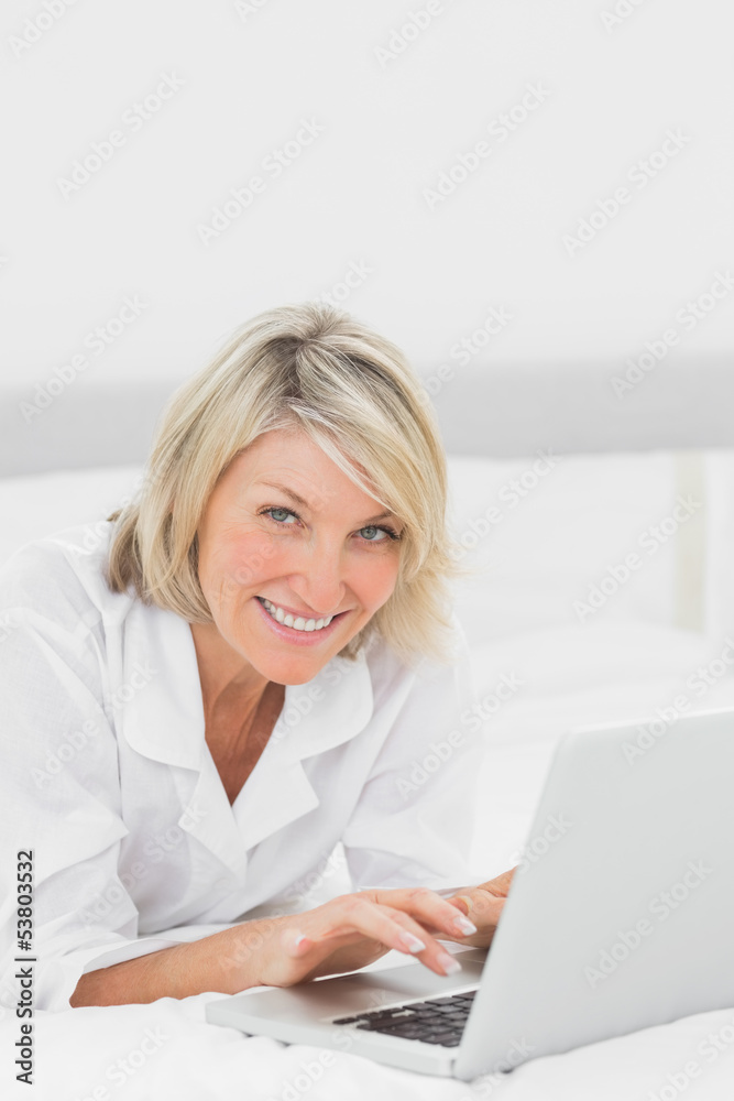 Happy woman using her laptop on her bed looking at camera Happy woman using her laptop on her bed looking at camera