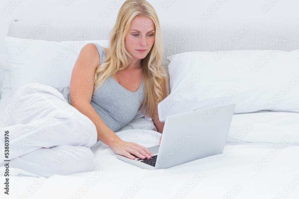 Woman lying on her bed using a laptop Woman lying on her bed using a laptop