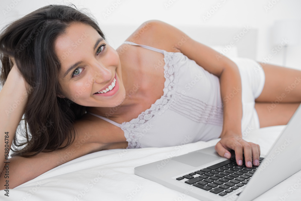 Cheerful woman using her laptop lying in bed Cheerful woman using her laptop lying in bed