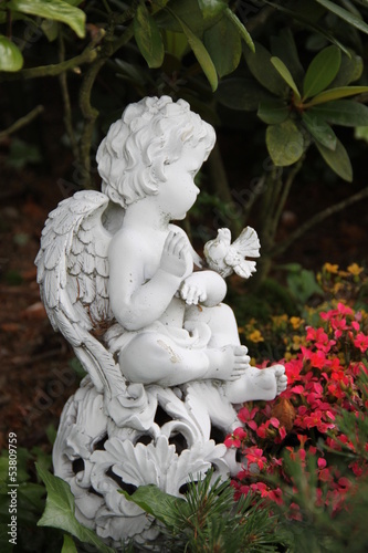 Kleiner Engel mit Taube sitzt auf bepflanztem Grab