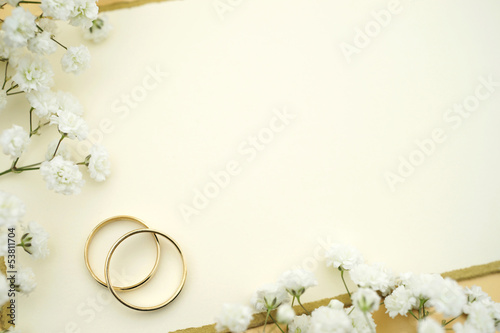 Elegante Hochzeitseinladung mit Eheringen aus Gold, einer Karte mit Textfreiraum und weissen Blumen. Copy space
