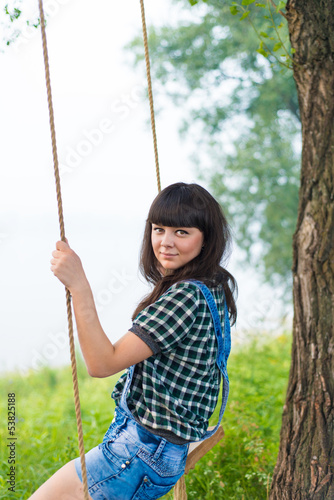 Portrait of pretty brunette swinging on rope swing