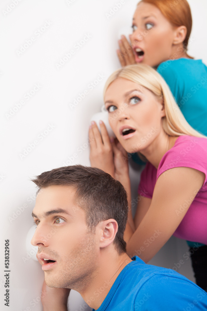 Fototapeta premium Can you hear that? Three young people eavesdropping near the wal