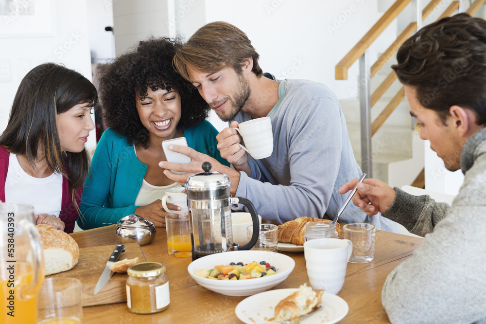 Friends sitting at a dining table and looking at a mobile phone Friends sitting at a dining table and looking at a mobile phone