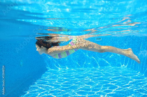 Happy child swims underwater in pool, fun on family vacation