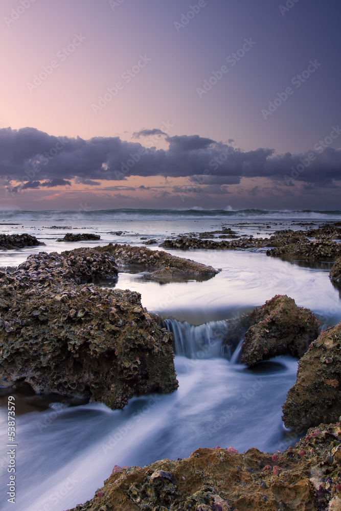 Sunrise landscape of ocean with waves clouds and rocks