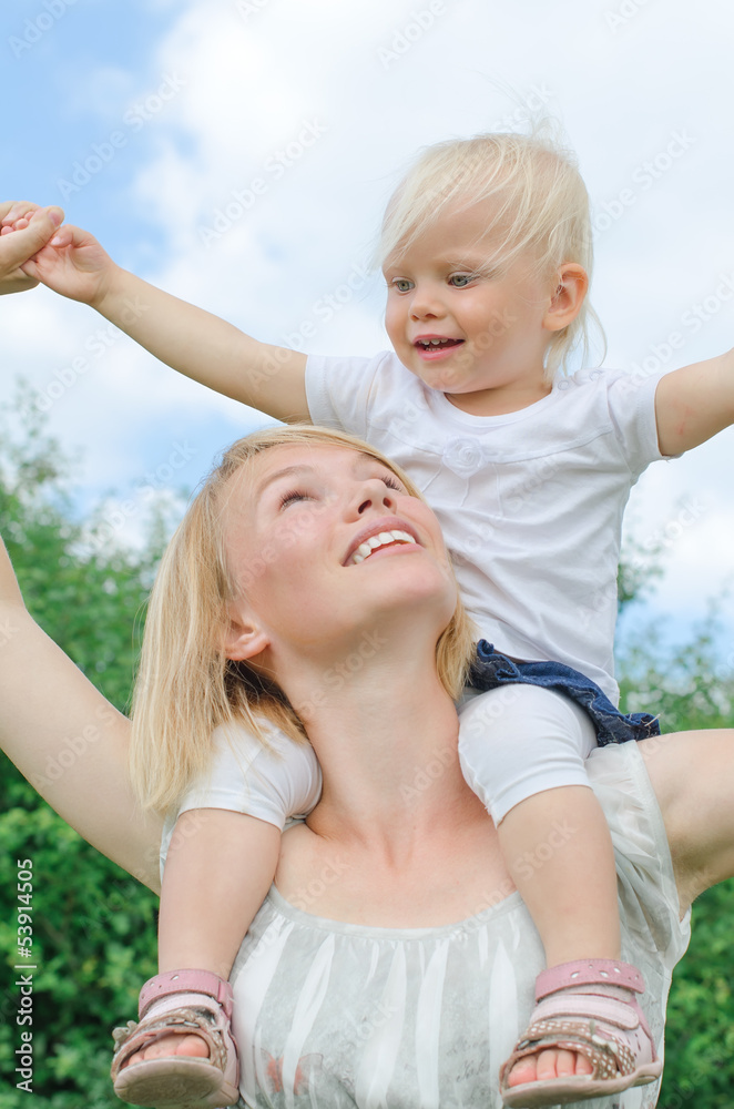 Fototapeta premium Happy mother carrying her daughter on shoulders