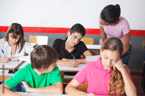 Teacher Assisting Teenage Schoolboy During Examination