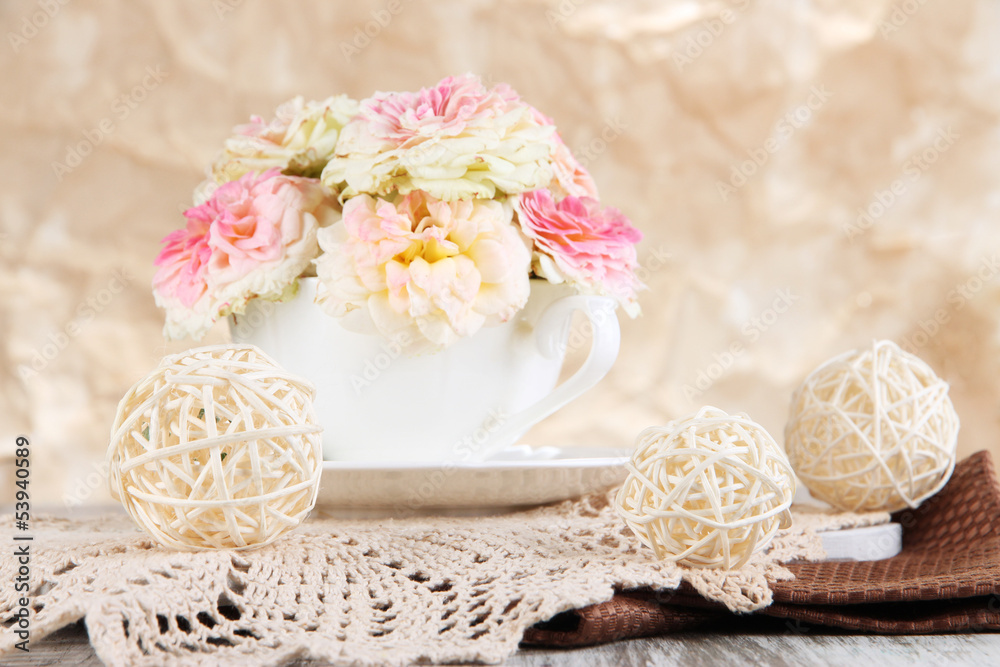 Roses in cup on napkins on wooden table on beige background Roses in cup on napkins on wooden table on beige background