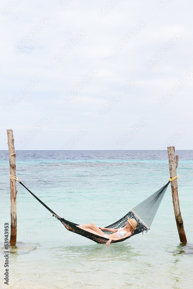 Woman Wearing Bikini And Sun Hat Relaxing In Beach Hammock