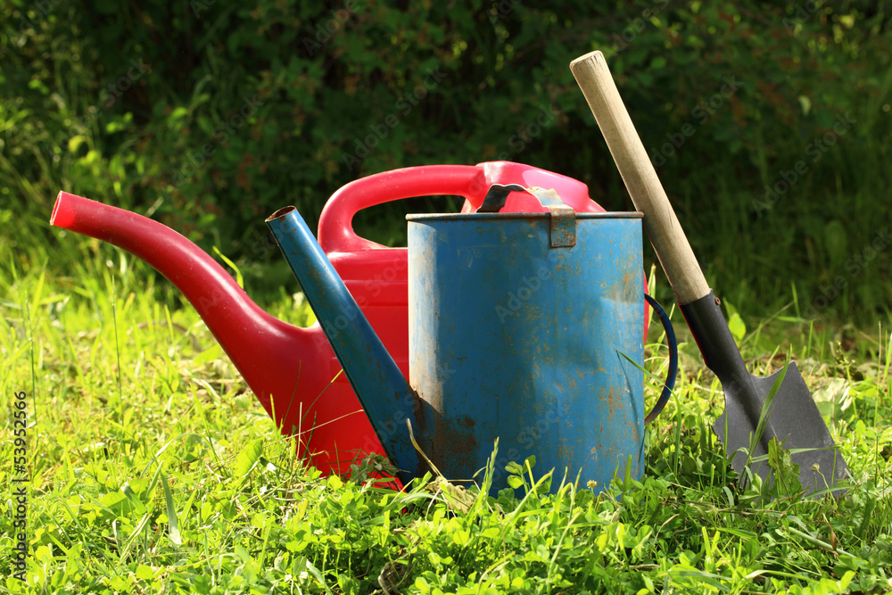 Old watering cans and shovel on grass Old watering cans and shovel on grass
